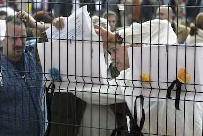 Varios votantes consultan sus nombres en el censo electoral colgado a las puertas del colegio Madrid Sur, frente a la estación de El Pozo. Junto a las listas, crespones negros y flores.