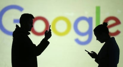 Dos personas navegan por el móvil con el logo de Google detrás. 