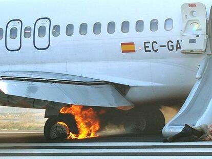 Un pasajero permanece herido en el suelo, junto a la rampa de emergencia, cuando todavía arde la rueda del avión.