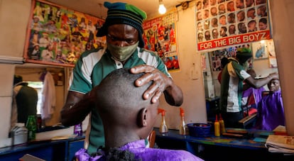 Un peluquero, protegido con mascarilla, afeita a su cliente dentro de una barbería llamada Old Trafford, dentro del barrio marginal de Kibera, en Nairobi (Kenia).