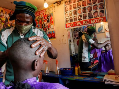 Un peluquero, protegido con mascarilla, afeita a su cliente dentro de una barbería llamada Old Trafford, dentro del barrio marginal de Kibera, en Nairobi (Kenia).
