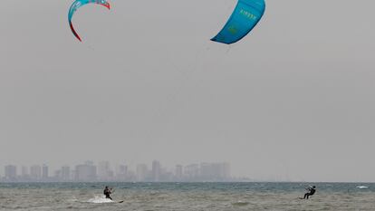 Dos personas practican kitesurf bajo un cielo plomizo en la Malvarrosa.