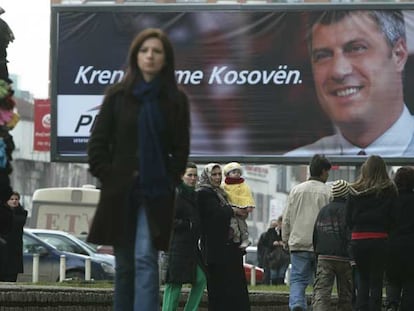 Ciudadanos de Pristina caminan frente a un cartel electoral del Partido Democrático de Kosovo.