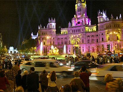 Decenas de viandantes se agolpan ante la fuente de la Cibeles para ver la iluminación nocturna especial con motivo de la boda real.