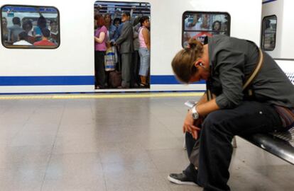 Un pasajero, sentado en un banco, mientras un convoy repleto de pasajeros se dispone a abandonar la estación.