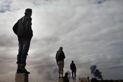 Combatientes anti-Gadafi, encaramados a unas columnas, observan la columna de humo causada por una explosión en un oleoducto cerca de Ras Lanuf.