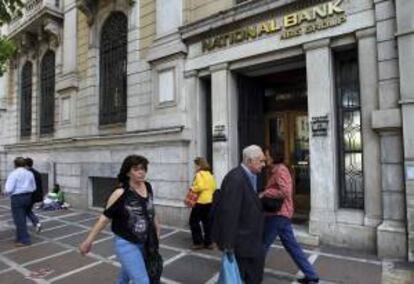 Varias personas caminan junto a una sucursal del National Bank de Grecia en Atenas, Grecia. EFE/Archivo