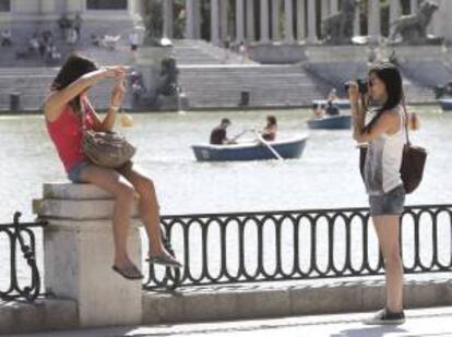 Dos turistas se fotografían en el parque del Retiro mientras otros pasean en barca. EFE/Archivo