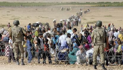 Kurdos sirios aguardan, frente a soldados turcos, en la valla fronteriza en Suruc, el 19 de septiembre