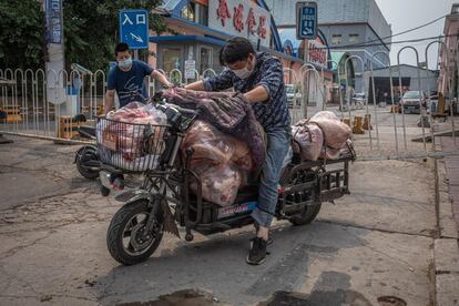 Una pareja de trabajadores carga un 'scooter' con carne al lado del edificio cerrado del mercado Xinfadi en Pekín (China).