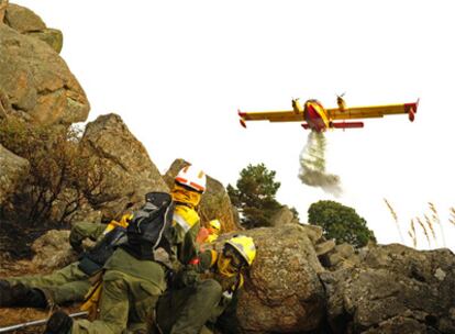 Varios bomberos se protegen entre las rocas al paso de un avión que trata de extinguir el incendio en Collado Mediano.
