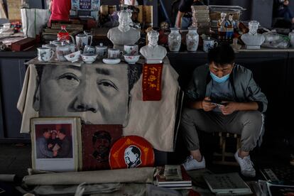 Un hombre con mascarilla vende recuerdos de la era de Mao en un mercado de Pekín