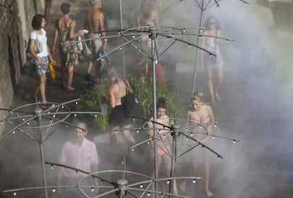 Varios hombres y mujeres aprovechan para refrescarse con agua pulverizada durante su paseo por París (Francia).