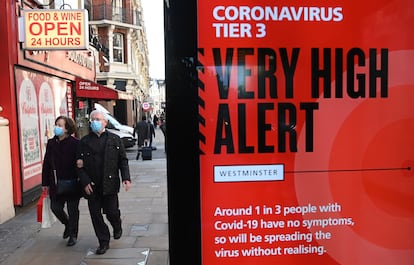 Pedestres passam diante de anúncio do Governo britânico sobre o coronavírus, hoje em Londres.