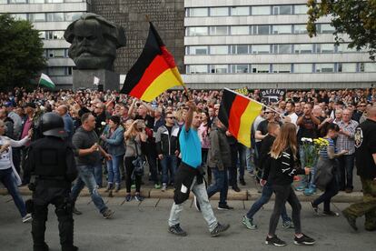 Gente sosteniendo banderas alemanas llegan a una protesta de derechas reunidos cerca de una estatua de Karl Marx.
