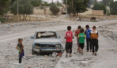 Hasan (de rojo) y sus amigos pasan junto a un coche destrozado en la ciudad siria de Al-Tabqa, en mayo de 2017. Hasan y su familia han tenido que cambiar de ciudad dos veces debido a la violencia, lo que le obligó a dejar la escuela en el grado 3.   