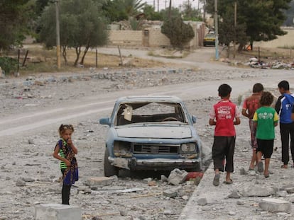 Hasan (de rojo) y sus amigos pasan junto a un coche destrozado en la ciudad siria de Al-Tabqa, en mayo de 2017. Hasan y su familia han tenido que cambiar de ciudad dos veces debido a la violencia, lo que le obligó a dejar la escuela en el grado 3.   