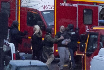 Oficial de segurança conduz reféns libertados (um deles com uma criança nos braços) depois que um homem armado tomar um supermercado kosher em Paris.