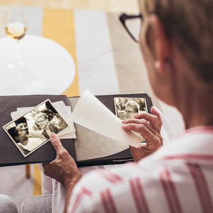 Cheerful senior female holding family photo album sitting on sofa at home