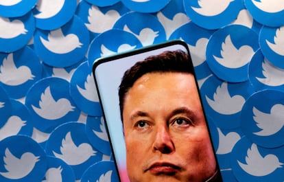 Imagen de Elon Musk en una pantalla sobre pegatinas con el logo de Twitter.