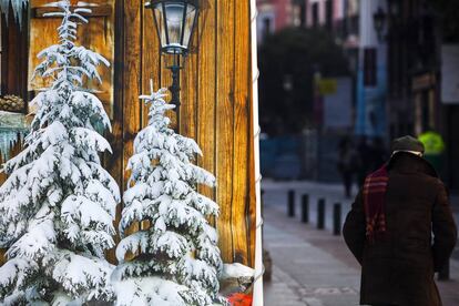 Un anciano pasa junto a unos abetos con nieve pintados en una calle de Madrid.