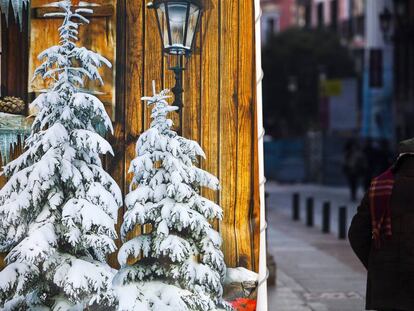 Un anciano pasa junto a unos abetos con nieve pintados en una calle de Madrid.