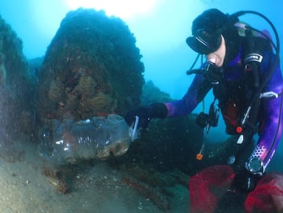 Un buzo recoge una botella de plástico del fondo marino.