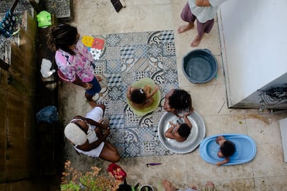 Isis Abena, de 35 años, y su hija Ainá, de dos, en el patio con sus vecinos en Salvador, Bahía. Durante los primeros meses de pandemia vivían en un departamento, pero con el confinamiento, el pequeño espacio empezó a afectar el humor de Ainá y la productividad de la madre. Las dos se mudaron a una casa de villa, donde la niña tiene más espacio, libertad, amigos y contacto con la naturaleza y donde Abena cuenta con una red de apoyo gracias a las otras familias que ahí viven. Entre todos se ayudan para cuidar a los niños.