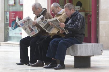 Un grupo de jubilados lee la prensa en una calle peatonal de Málaga.