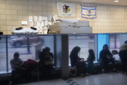 Immigrants from Venezuela are reflected in a marble wall while taking shelter at the Chicago Police Department's 16th District station on Monday, May 1, 2023