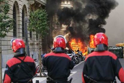 Tres <i>ertzainas</i> observan unos contenedores ardiendo en la calle Hondarribia, en el centro de San Sebastián, ayer por la tarde.
JESÚS URIARTE