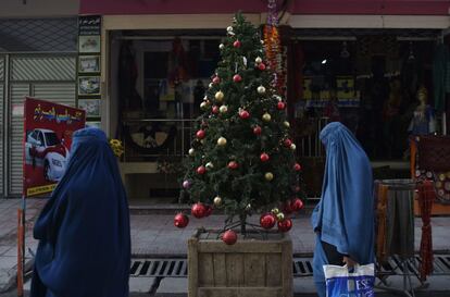 Mujeres afganas con burka pasan junto a un árbol de Navidad en una calle de Kabul, el 24 de diciembre de 2018.