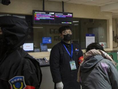 Un trabajador que usa un traje de materiales peligrosos utiliza un termómetro digital para revisar a un pasajero en una estación de metro en Beijing