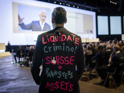 Un hombre viste un traje con la leyenda "Liquidate Criminal Suisse + Banksters Assets", mientras el presidente del banco suizo, Axel P. Lehmann, habla durante la junta anual de accionistas del grupo.