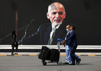 Pasajeros en el aeropuerto de Kabul pasan junto a la imagen del por entonces presidente de Afganistán, Ashraf Ghani, el 14 de agosto, con los talibanes ya cercando la capital.