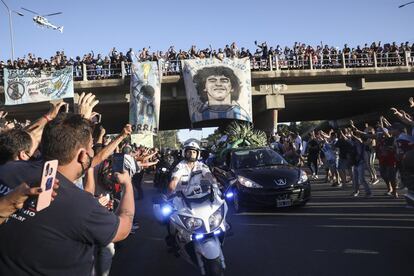 Cientos de aficionados saludan desde un paso elevado al coche fúnebre que lleva los restos de Diego Armando Maradona.