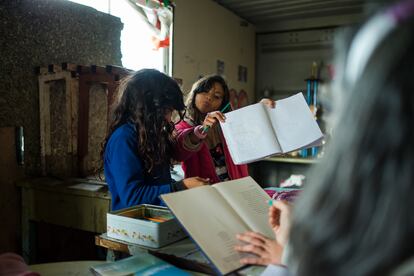 Dos niñas del barrio Nueva Esperanza muestran sus ejercicios a la maestra que brinda apoyo escolar.