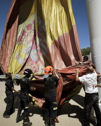 Operarios municipales y miembros de la Armada alzan la bandera tras su caída al suelo.