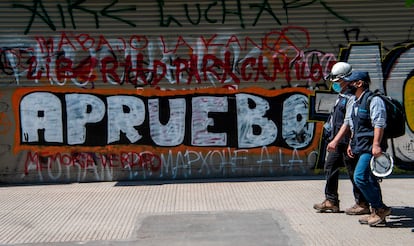 Homens passam diante de um grafite em Santiago do Chile que convoca a população a votar em favor da reforma constitucional no próximo domingo.