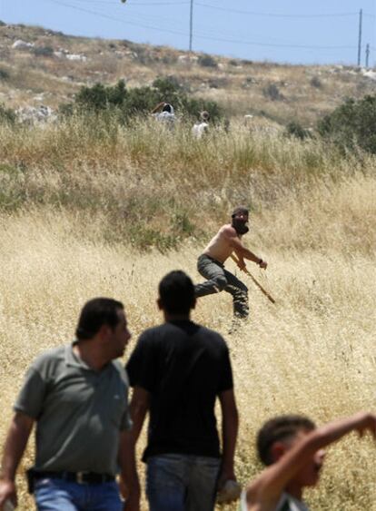 Un colono israelí lanza una piedra contra unos palestinos.