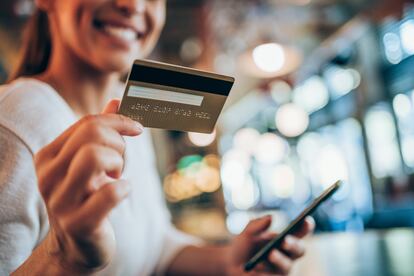 Woman using smart phone and credit card for online shopping in city cafe.