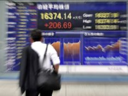 Un hombre de negocios observa varios valores burs&aacute;tiles mostrados en una calle de Tokio (Jap&oacute;n).