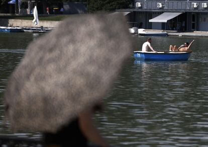 Una mujer con un paraguas con un paraguas junto al estanque del Retiro, este lunes durante la ola de calor en Madrid. 