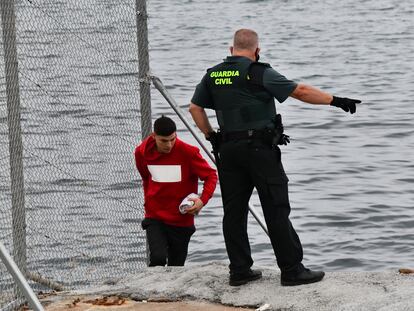 Un Guardia Civil observa a uno de los inmigrantes en uno de los espigones fronterizos de Ceuta.