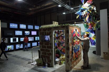 Mezcla de materiales (pantalla de plasma, papel, ladrillo, vidrio…) en el stand de EL PAÍS, que rinde tributo al arte urbano más allá del tópico. A la derecha, 3ttman aplica su spray a una de las piezas del puzle.