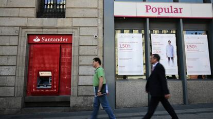 Dos viandantes pasan frente a una sucursal del Banco Santander y una del Banco Popular en Madrid.