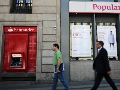 Dos viandantes pasan frente a una sucursal del Banco Santander y una del Banco Popular en Madrid.