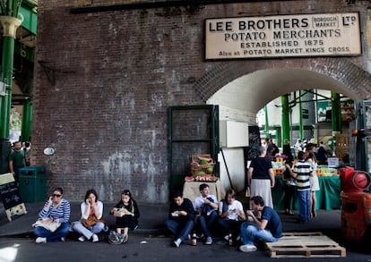 El mercado gastronómico más famoso de Londres ocupa una serie de patios conectados bajo las vías elevadas del ferrocarril, en el distrito Southwark (en el sudeste de la ciudad). Desde muy temprano acuden visitantes y locales, y es habitual que los comerciantes den a probar sus especialidades (queso frito, aceitunas o pan artesano mojado en salsas picantes) antes de que el comensal opte por algún plato más consistente para comer. Conocido popularmente como la despensa de Londres, este mercado ha existido de una forma u otra en el mismo lugar desde el siglo XVIII pero ha disfrutado de un renacimiento colosal en los últimos 15 años. No hay día que no esté repleto de amantes de la comida, gastrónomos de todos los rincones del mundo y visitantes curiosos, pero también de londinenses en busca de inspiración. Se ha convertido, por derecho propio, en un destino turístico. El mercado está especializado en productos frescos de alta calidad, desde futas y verduras, quesos, carnes o pescados hasta panaderías o puestos <i>gourmet</i>. Destacan especialmente los puestos de repostería. Es todo un espectáculo suculento y vistoso al que muchos acuden cámara en mano. El precio es alto, como era de esperar en la capital británica, pero muchos comerciantes ofrecen muestras gratuitas. En la imagen, un grupo de jóvenes almuerza frente a un cartel de un antiguo negocio, debajo de las vías del tren.