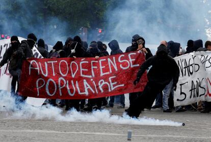 Gas lacrimógeno flota en el aire mientras los manifestantes marchan tras una pancarta que dice: "Autodefensa populista" durante los enfrentamientos en la marcha tradicional del sindicato de trabajadores, en París.