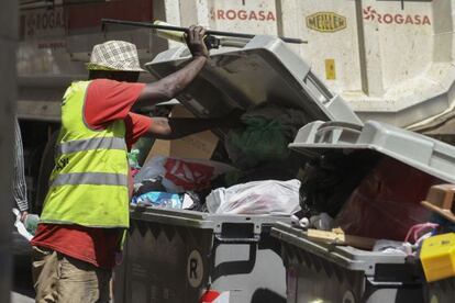 Un indigente remueve un contenedor de basura en Barcelona.